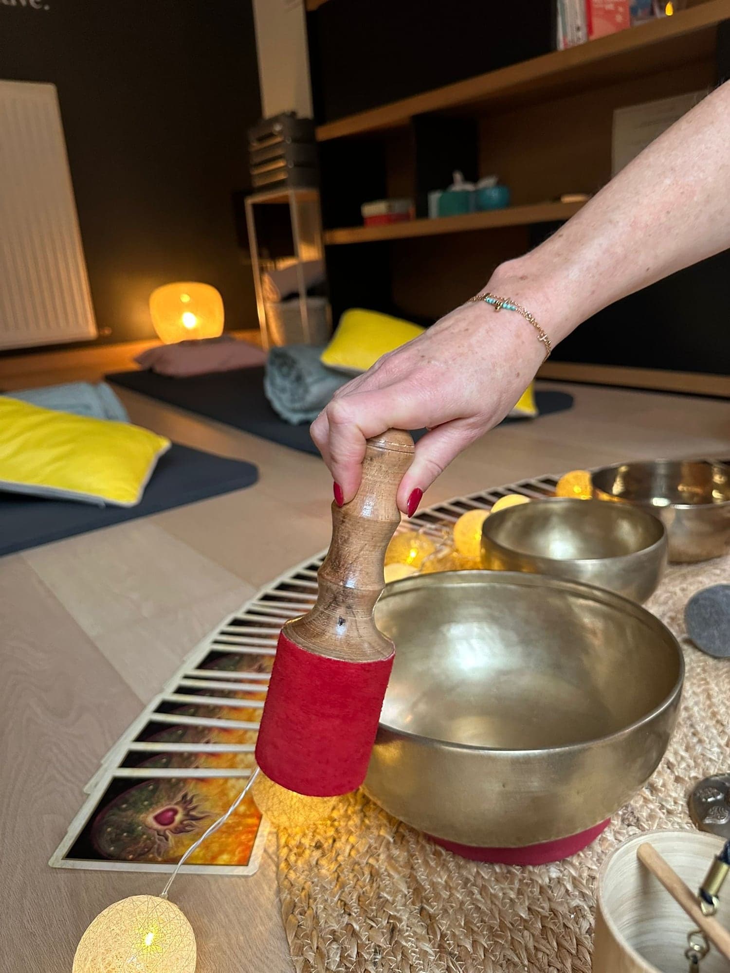 Une main fait résonner un bol tibétain avec un maillet, devant des tapis et des coussins préparés pour les participants