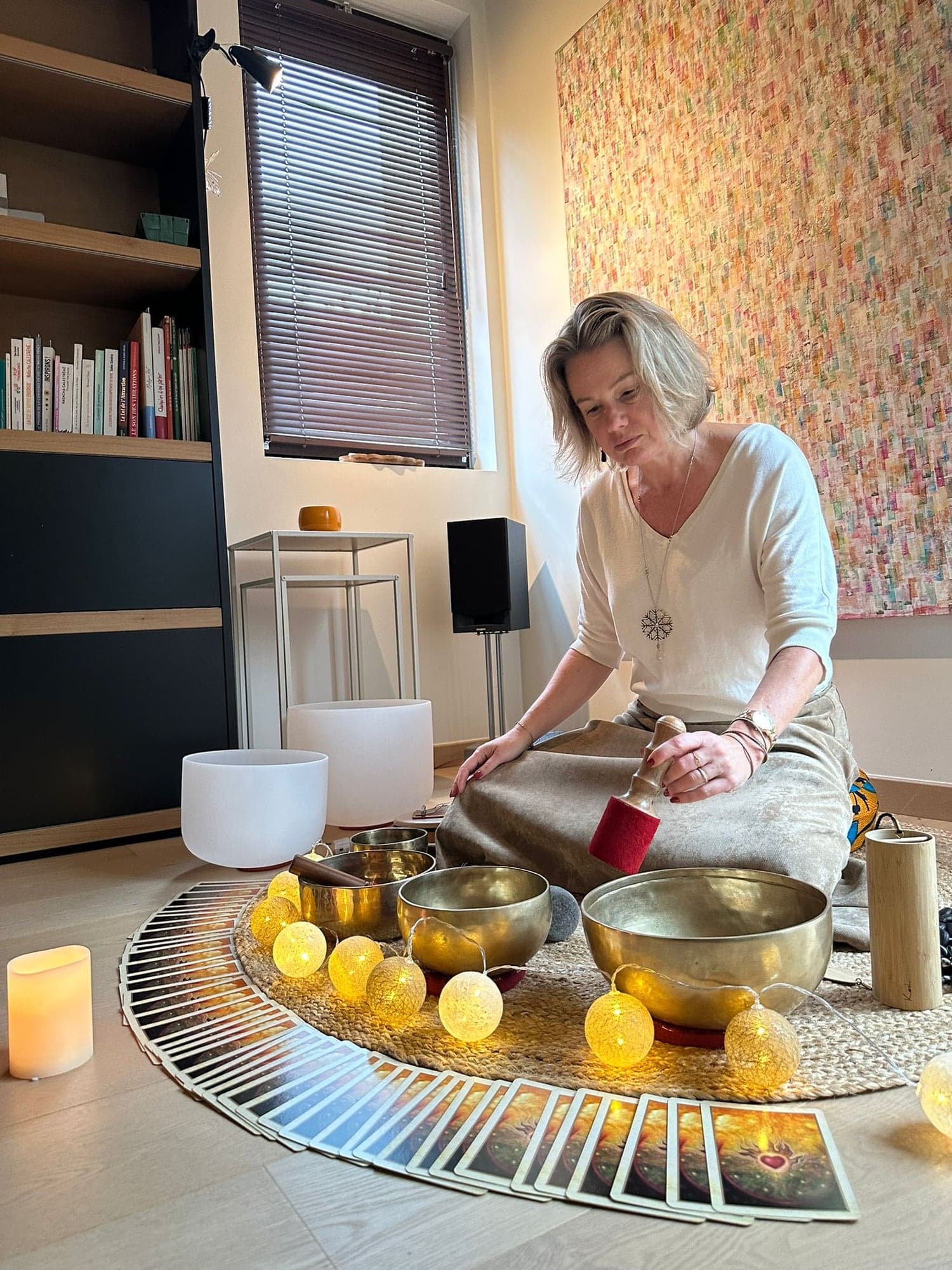 Catherine, assise au sol, fait chanter un bol tibétain, entourée de bols chantants et de petites lumières