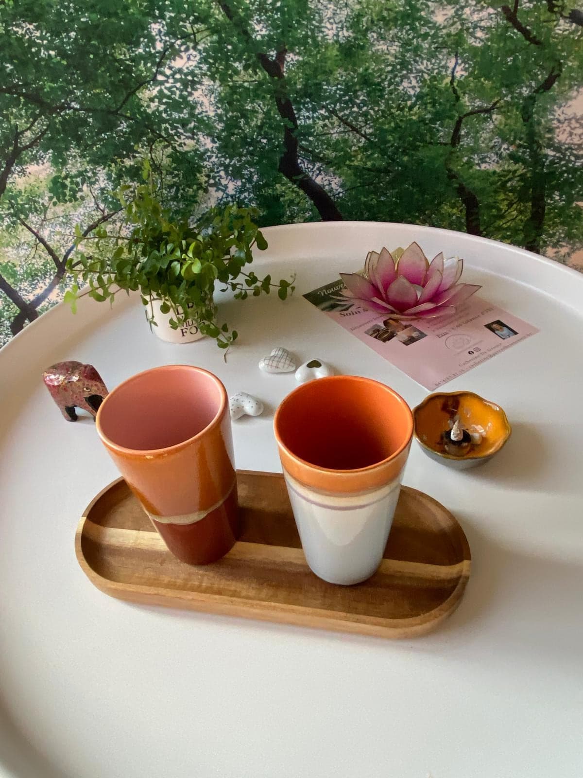 Un plateau avec deux tasses, une plante et une petite bougie, à côté d’un flyer orné d’une fleur de lotus