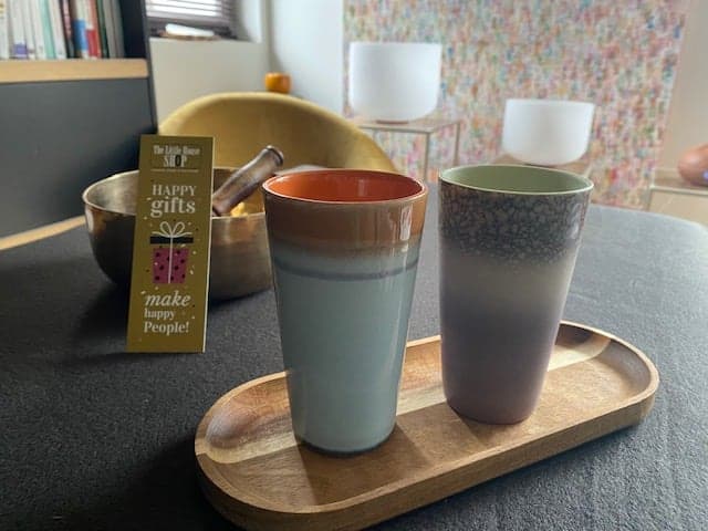 Deux tasses en céramique sur un plateau en bois, devant un bol tibétain