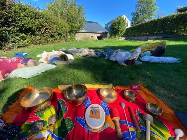 Un voyage sonore en plein air : des participant·es allongé·es dans l’herbe, devant des bols tibétains et d’autres instruments posés sur une étoffe colorée