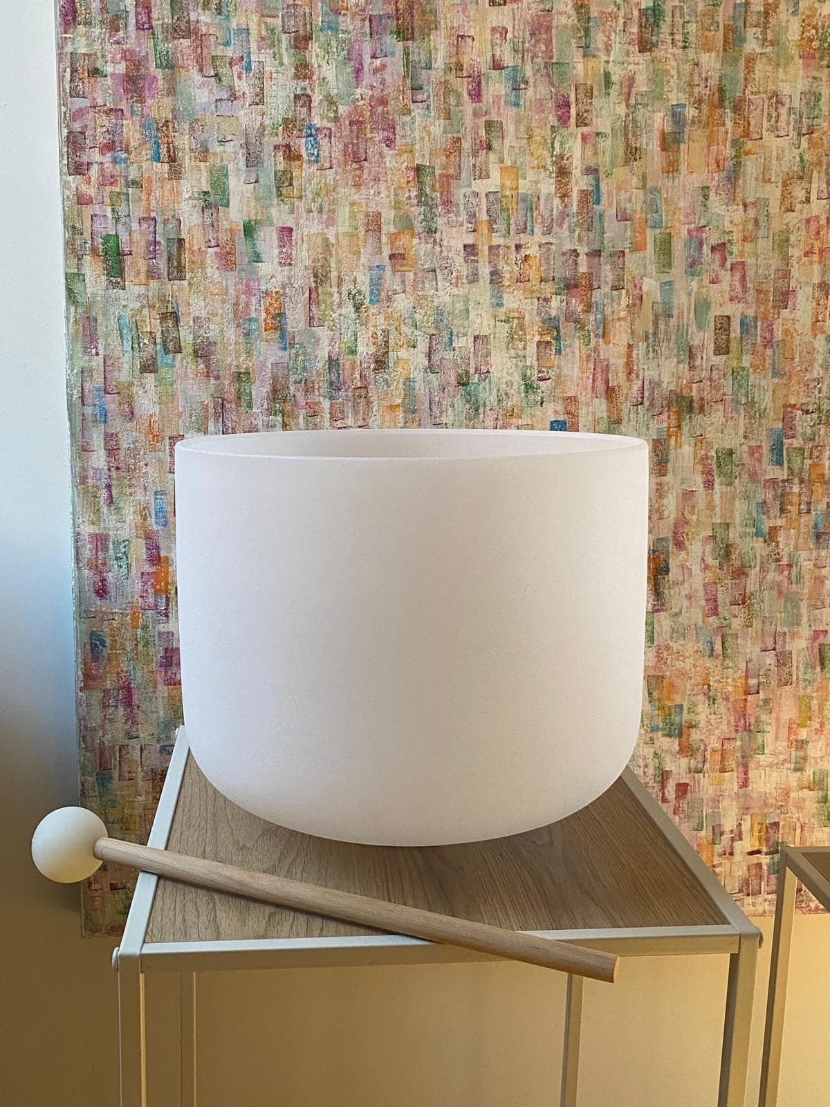 Un grand bol de cristal blanc et son maillet, devant une toile aux couleurs douces